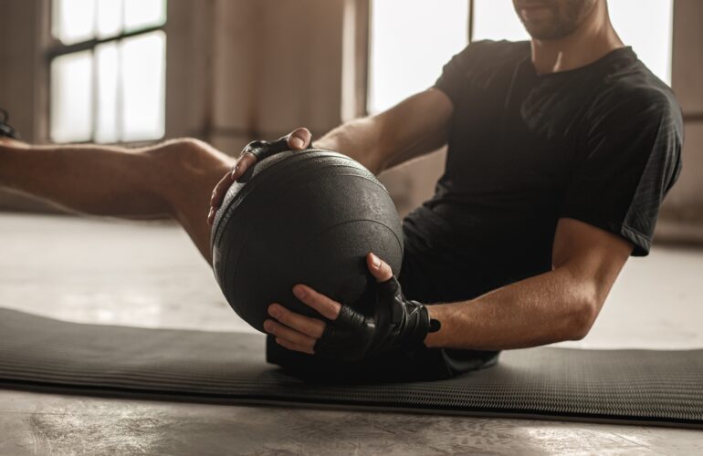 Side view of crop unrecognizable athletic male doing side twist exercise with medicine ball during intense functional training in gym